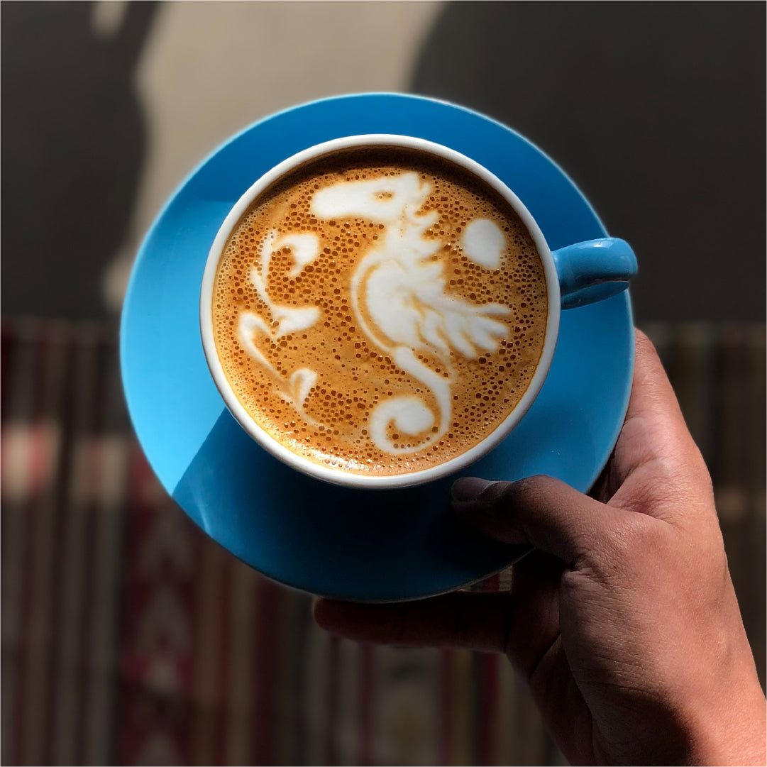 Hand holding a blue cup with seahorse latte art