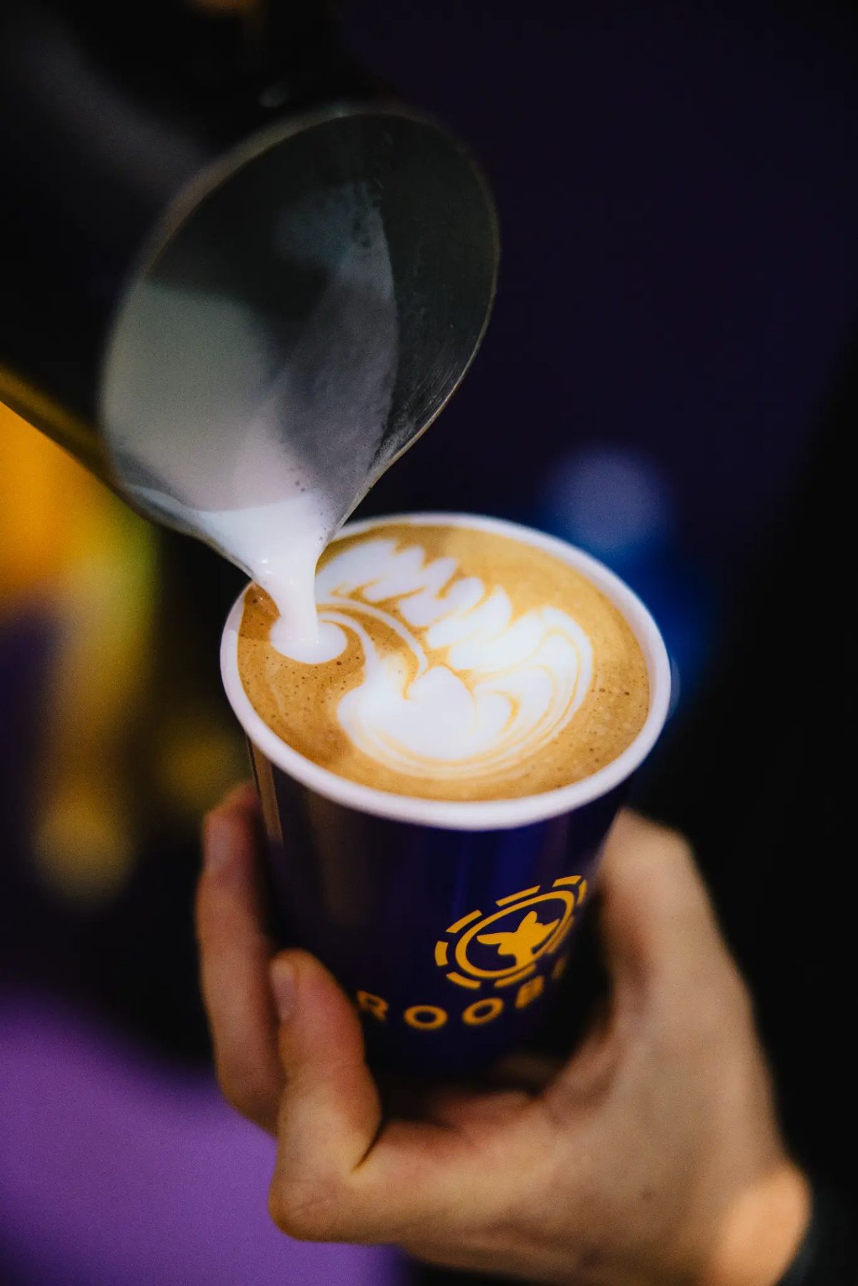 Barista pouring latte art into a branded cup